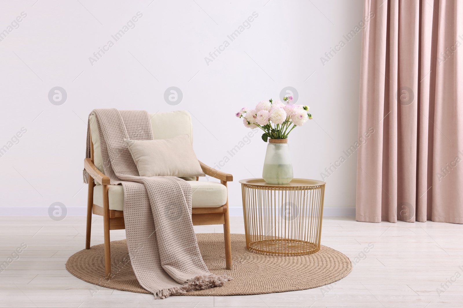 Photo of Comfortable armchair with blanket, pillow, table and beautiful flowers in room