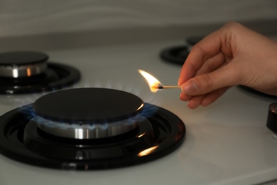 Photo of Woman lighting gas stove with match, closeup