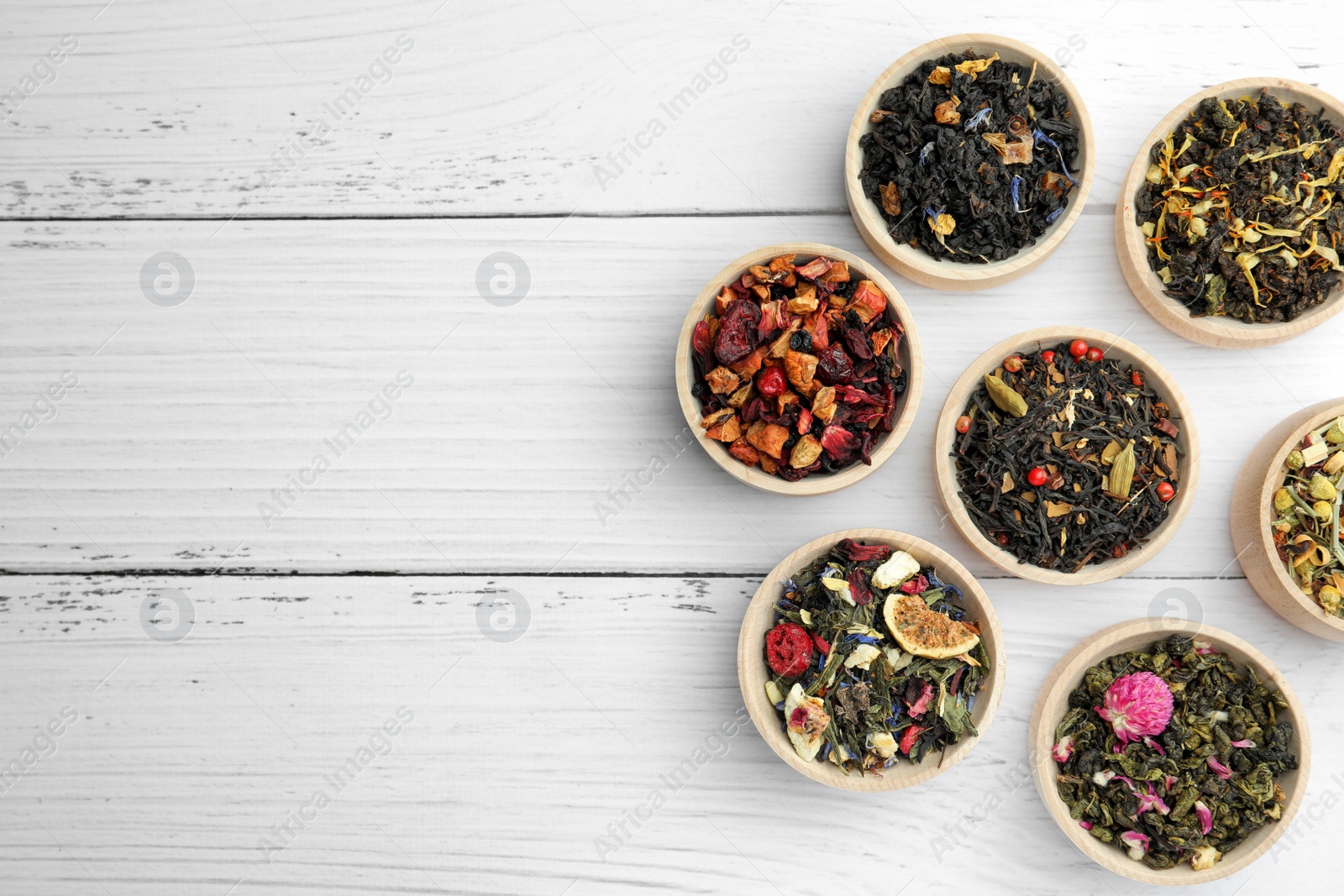 Photo of Different kinds of dry herbal tea in bowls on white wooden table, flat lay