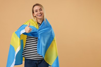 Happy woman with flag of Sweden showing thumbs up on beige background, space for text