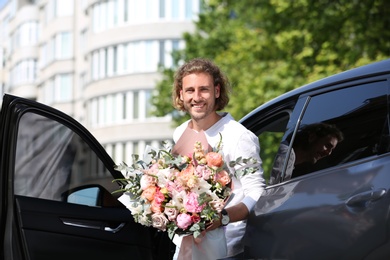 Photo of Young handsome man with beautiful flower bouquet near car on street