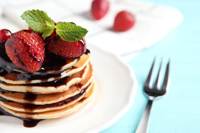 Delicious pancakes with fresh strawberries and chocolate syrup on light blue wooden table, closeup