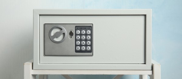 Image of Closed steel safe on white table against light blue background, banner design