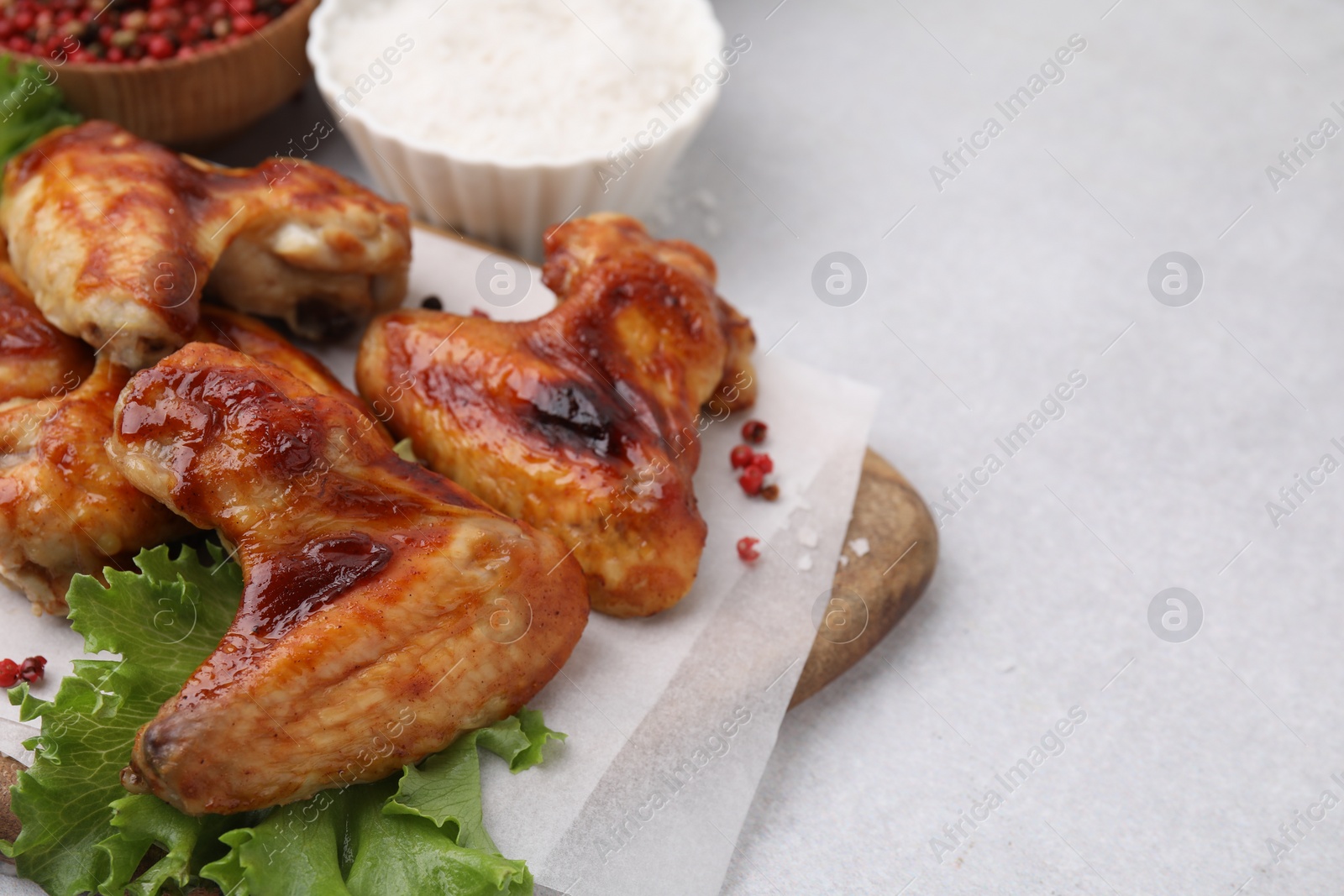 Photo of Fresh marinated chicken wings, spices and lettuce on light table, closeup. Space for text