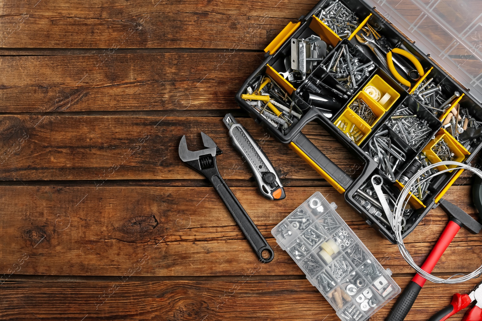 Photo of Plastic box with different bolts, nuts and tools on wooden table, flat lay. Space for text