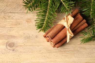 Bunch of cinnamon sticks and fir branches on wooden table, top view. Space for text