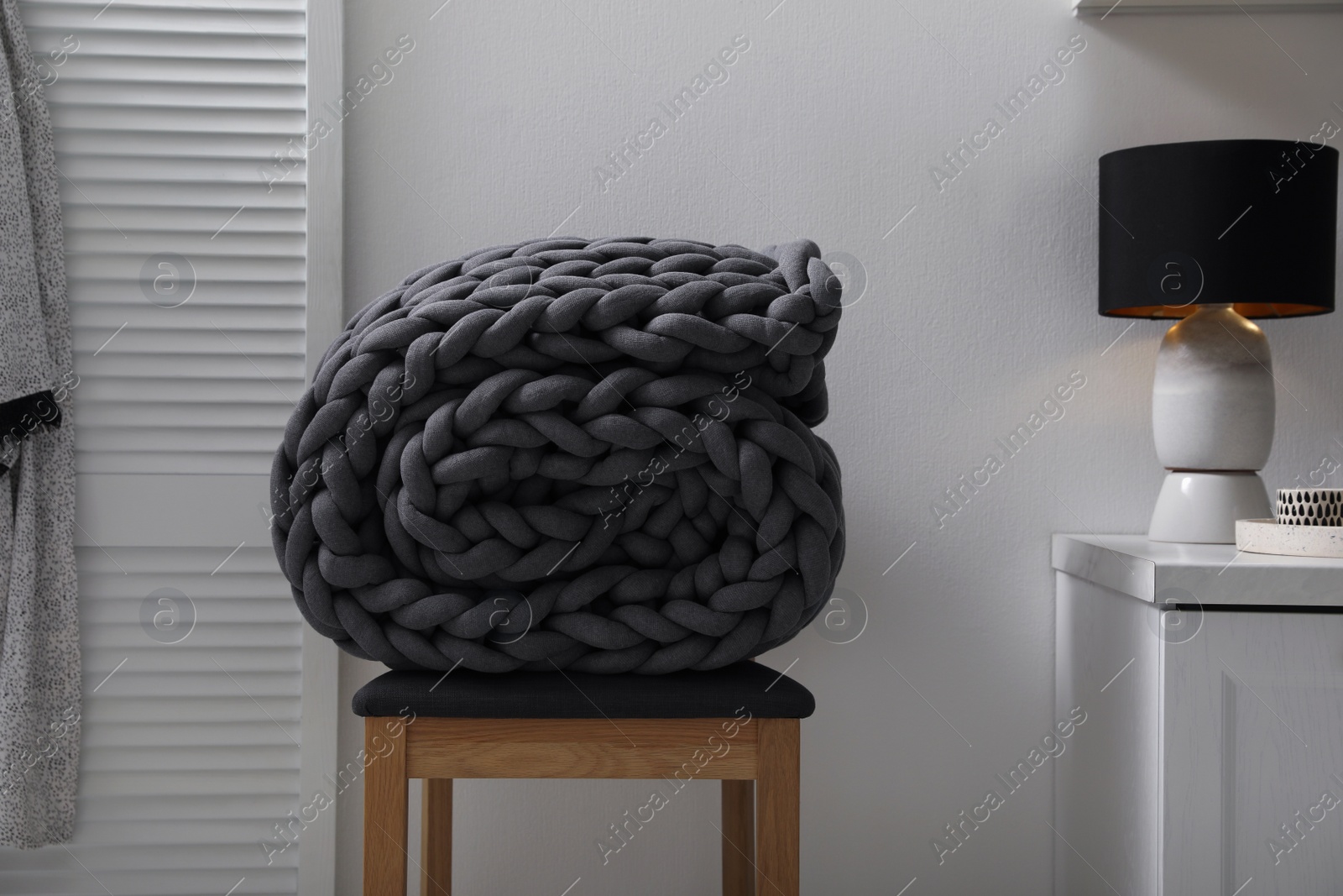 Photo of Dark grey chunky knit blanket rolled on wooden stool in room