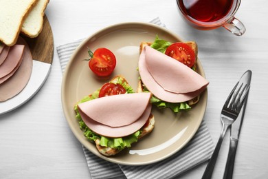 Photo of Plate of tasty sandwiches with boiled sausage, tomato and lettuce on white wooden table, flat lay