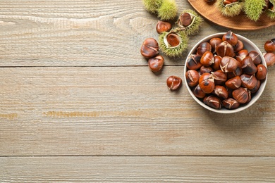 Photo of Delicious roasted edible chestnuts on wooden table, flat lay. Space for text