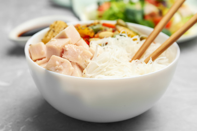 Photo of Tasty cooked rice noodles with chicken and vegetables on grey marble table, closeup