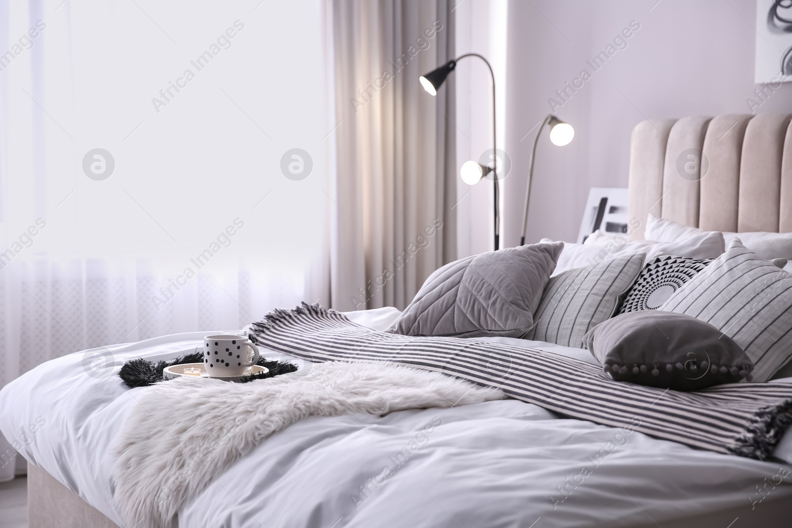 Photo of Bed with cushions and striped blanket in room. Interior design