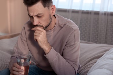 Upset man with glass of water in bedroom. Loneliness concept