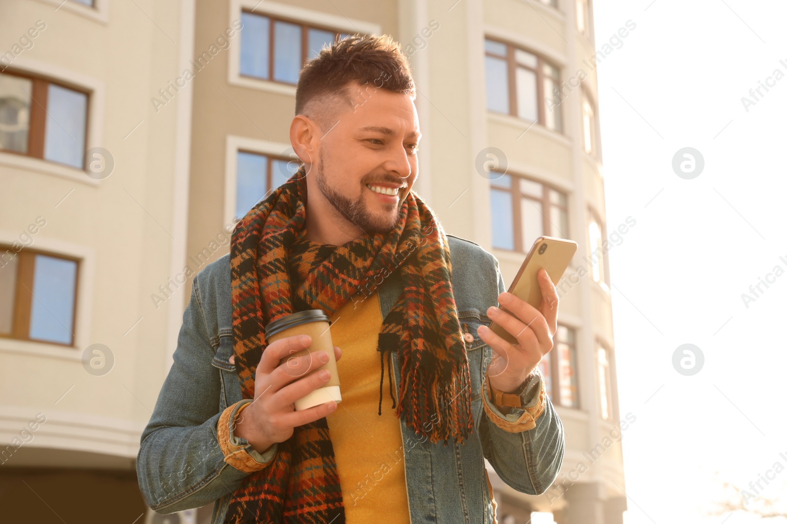 Photo of Man with cup of coffee and smartphone on city street in morning