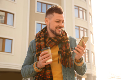 Photo of Man with cup of coffee and smartphone on city street in morning