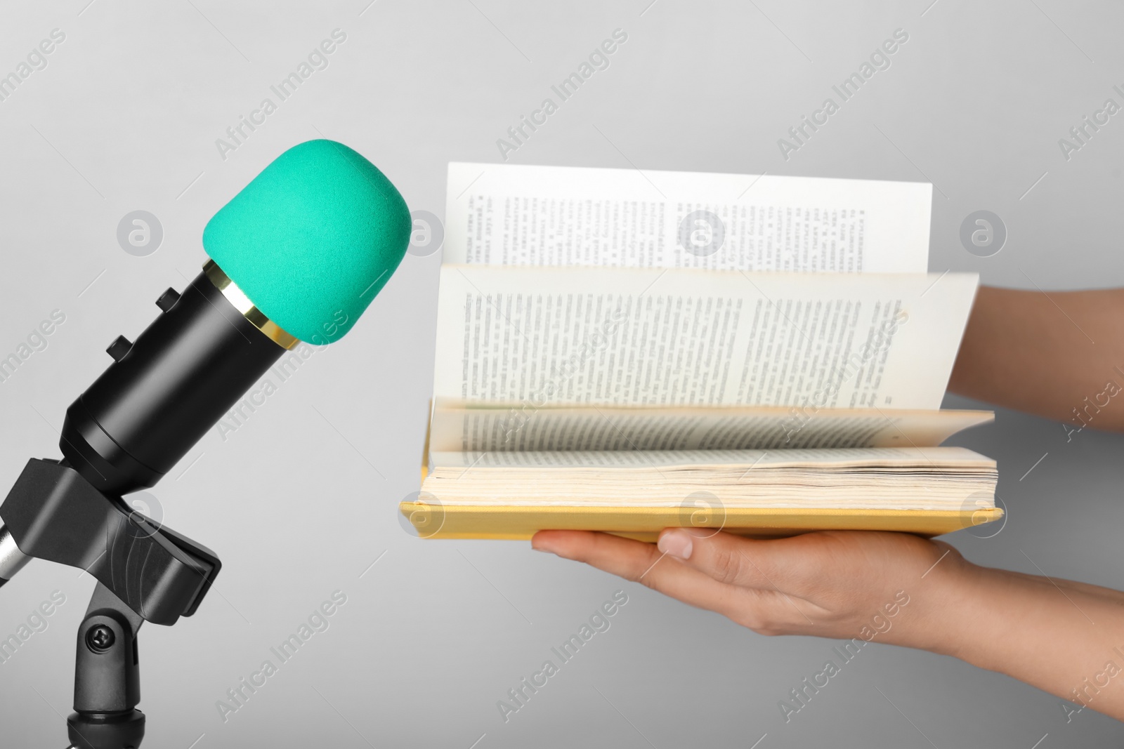 Photo of Woman making ASMR sounds with microphone and book on grey background, closeup