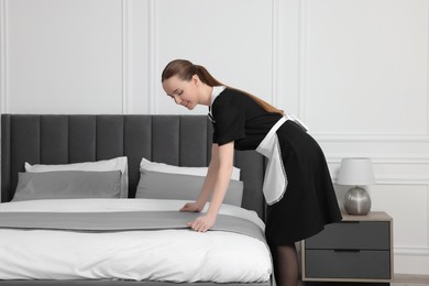 Young maid making bed in hotel room