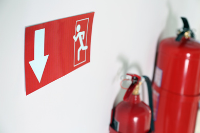 Photo of Emergency exit sign and fire extinguishers on white wall, closeup