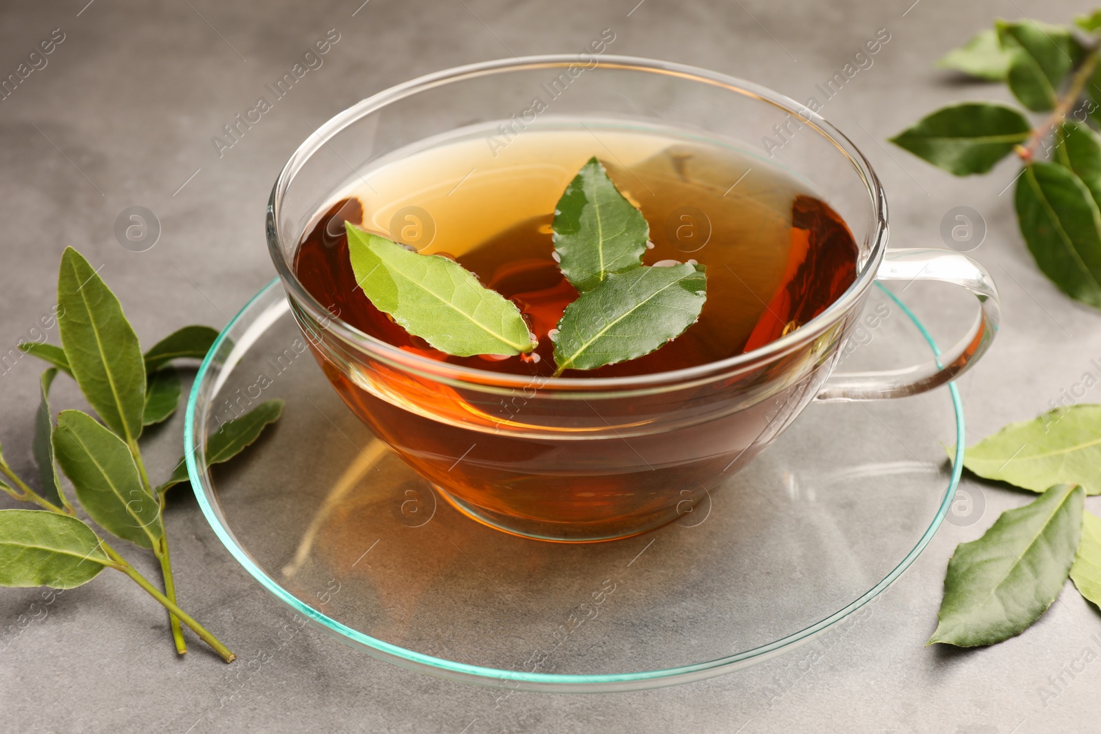 Photo of Cup of freshly brewed tea with bay leaves on grey table, closeup