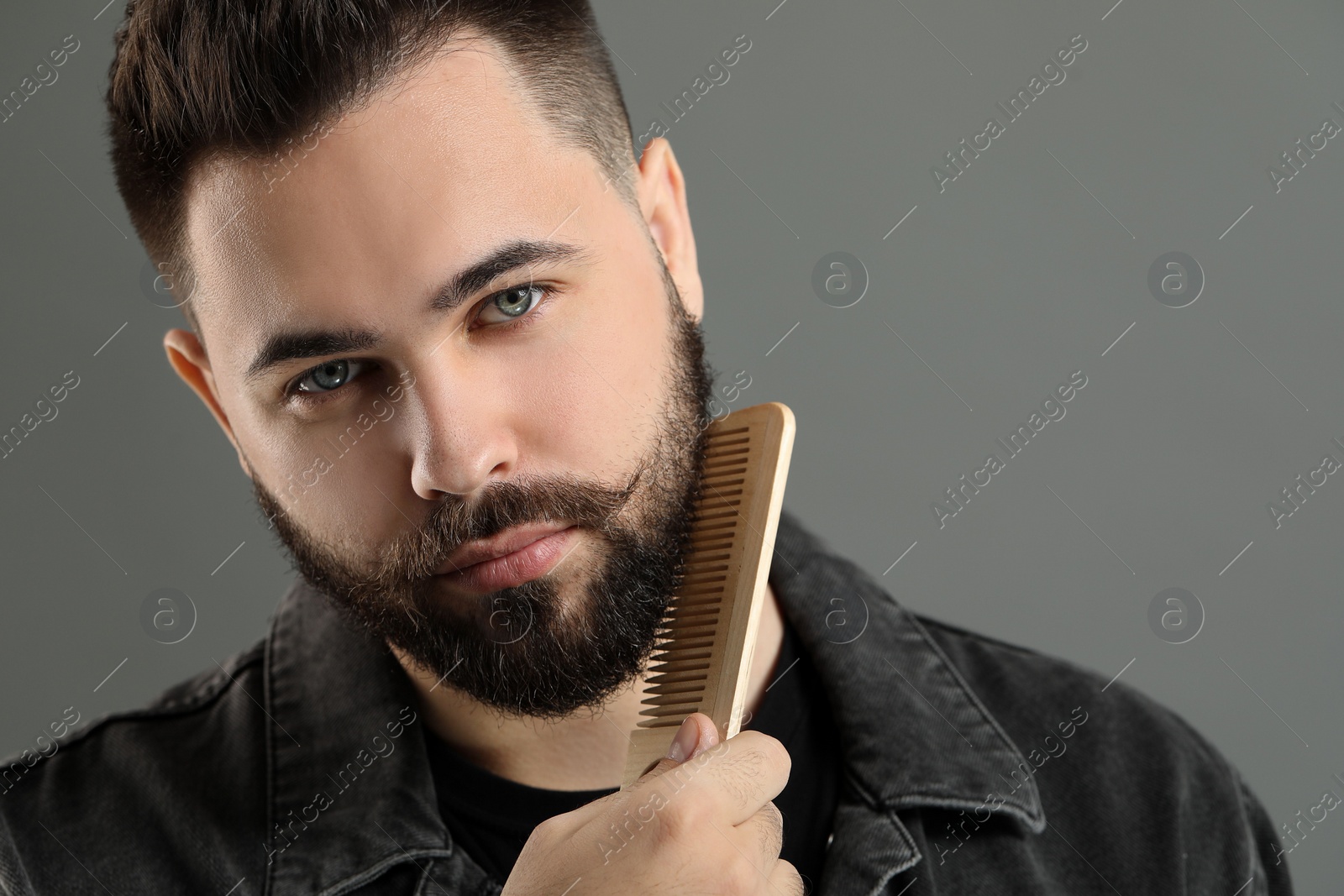 Photo of Handsome young man combing beard on grey background