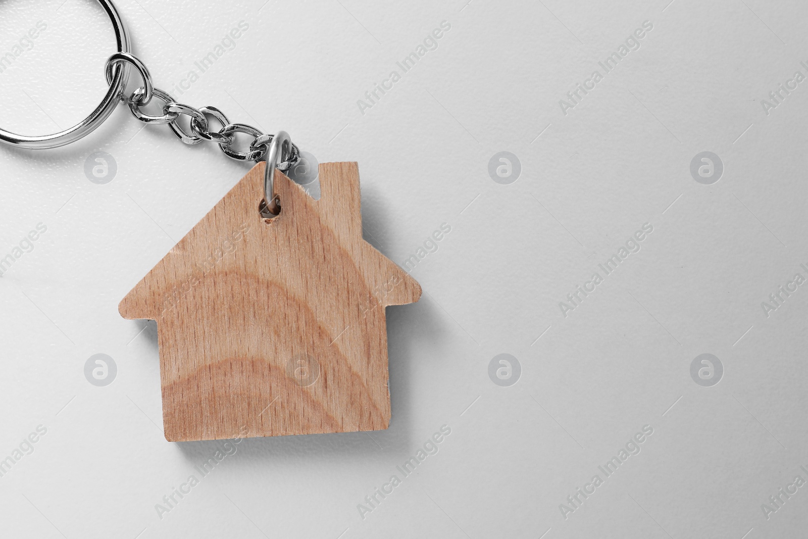 Photo of Wooden keychain in shape of house on light table, top view. Space for text