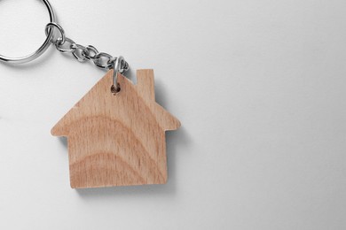 Photo of Wooden keychain in shape of house on light table, top view. Space for text