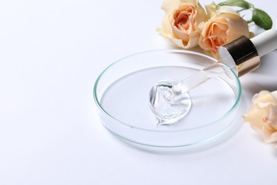 Photo of Petri dish with sample of cosmetic serum, pipette and rose flowers on white background, space for text