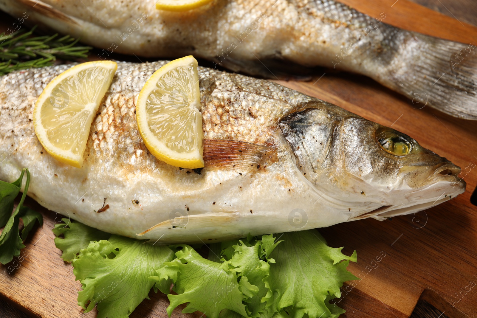 Photo of Delicious baked fish, lettuce and lemon on wooden board, closeup