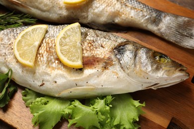 Photo of Delicious baked fish, lettuce and lemon on wooden board, closeup