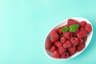 Bowl of delicious ripe raspberries on turquoise background, top view. Space for text