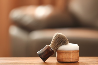 Shaving brush and foam on table against blurred background with space for text