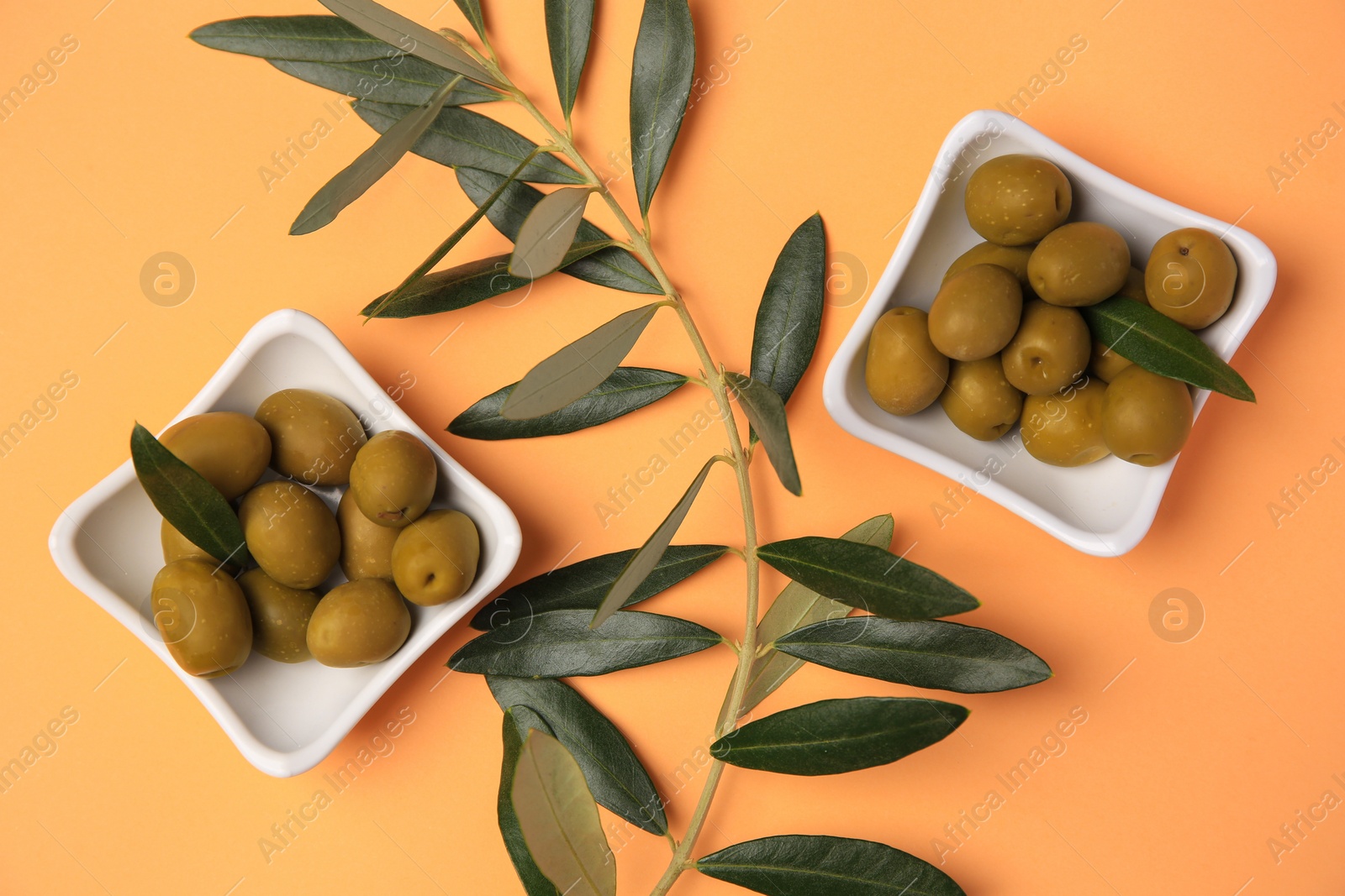 Photo of Fresh olives and green leaves on pale orange background, flat lay
