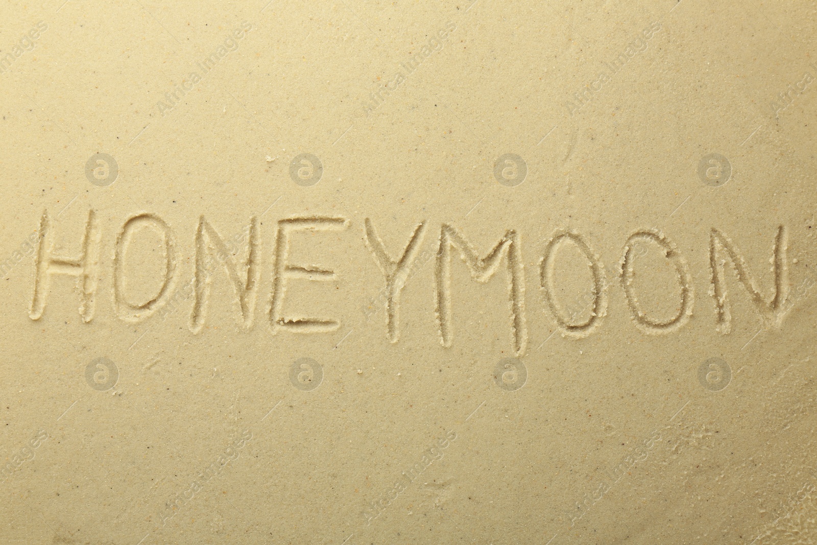 Photo of Word Honeymoon written on sand, top view