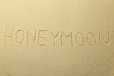 Photo of Word Honeymoon written on sand, top view