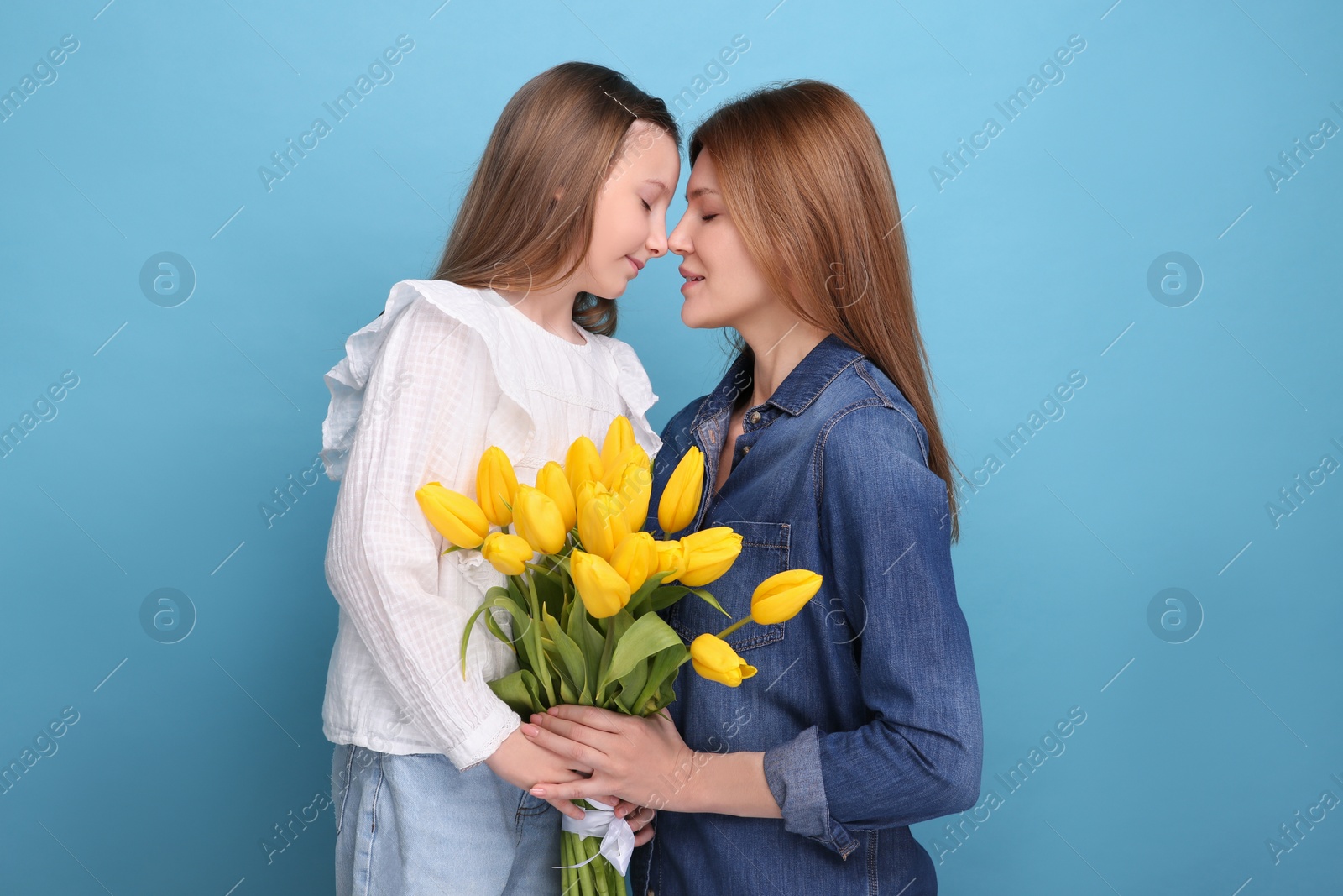 Photo of Mother and her cute daughter with bouquet of yellow tulips on light blue background