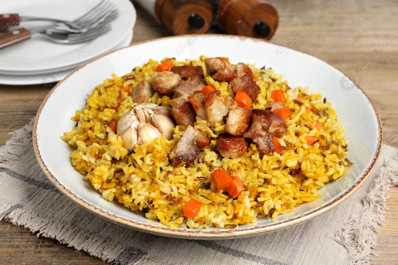 Photo of Delicious pilaf with meat, carrot and garlic on wooden table, closeup