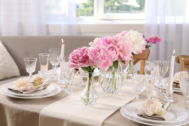 Stylish table setting with beautiful peonies and burning candles indoors