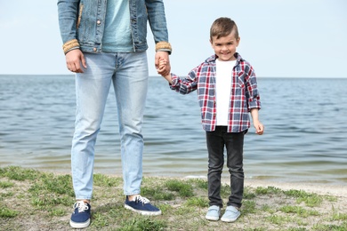 Photo of Cute little child holding hands with his father near river. Family time