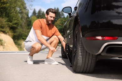 Photo of Man lifting car to change wheel on roadside outdoors