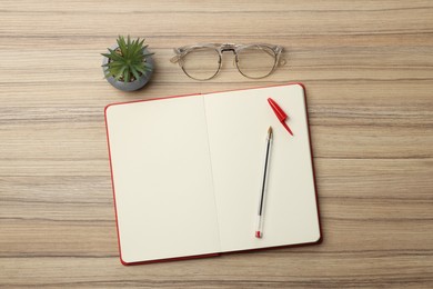 Photo of Ballpoint pen, notebook and glasses on wooden table, flat lay