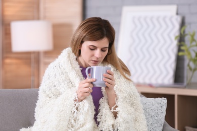 Photo of Sick woman with cup of hot drink suffering from cold on sofa at home