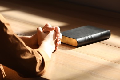 Religious woman praying over Bible indoors, closeup