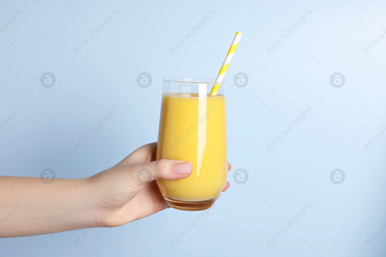 Photo of Woman holding glass of tasty smoothie on light blue background, closeup