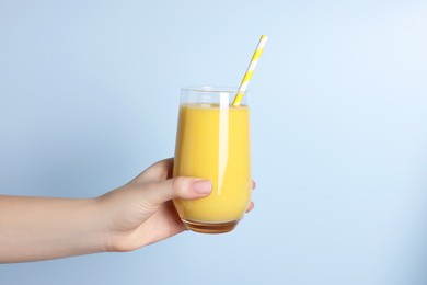 Woman holding glass of tasty smoothie on light blue background, closeup
