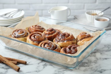 Photo of Baking dish with tasty cinnamon rolls and sticks on white marble table