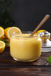 Delicious lemon curd in glass jar, fresh citrus fruits and spoon on wooden table