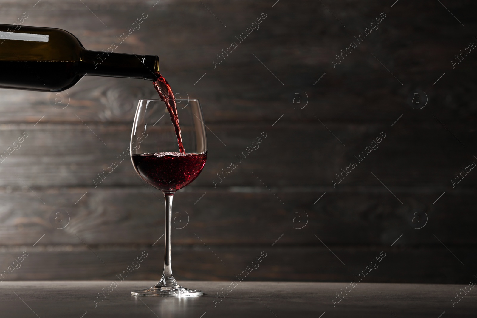 Photo of Pouring red wine into glass from bottle on table against wooden background. Space for text