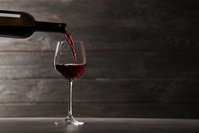 Photo of Pouring red wine into glass from bottle on table against wooden background. Space for text