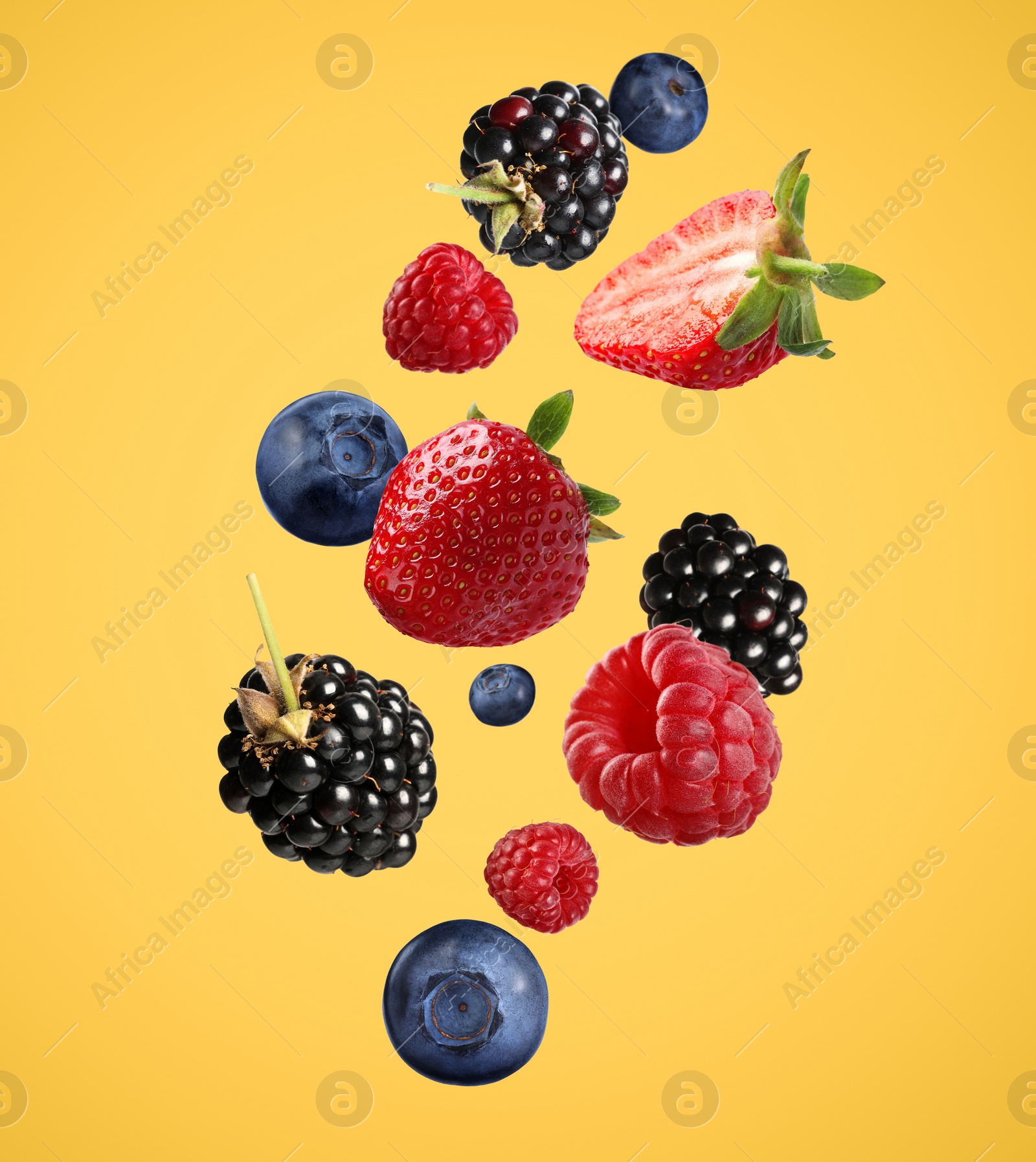 Image of Many different fresh berries falling on golden background