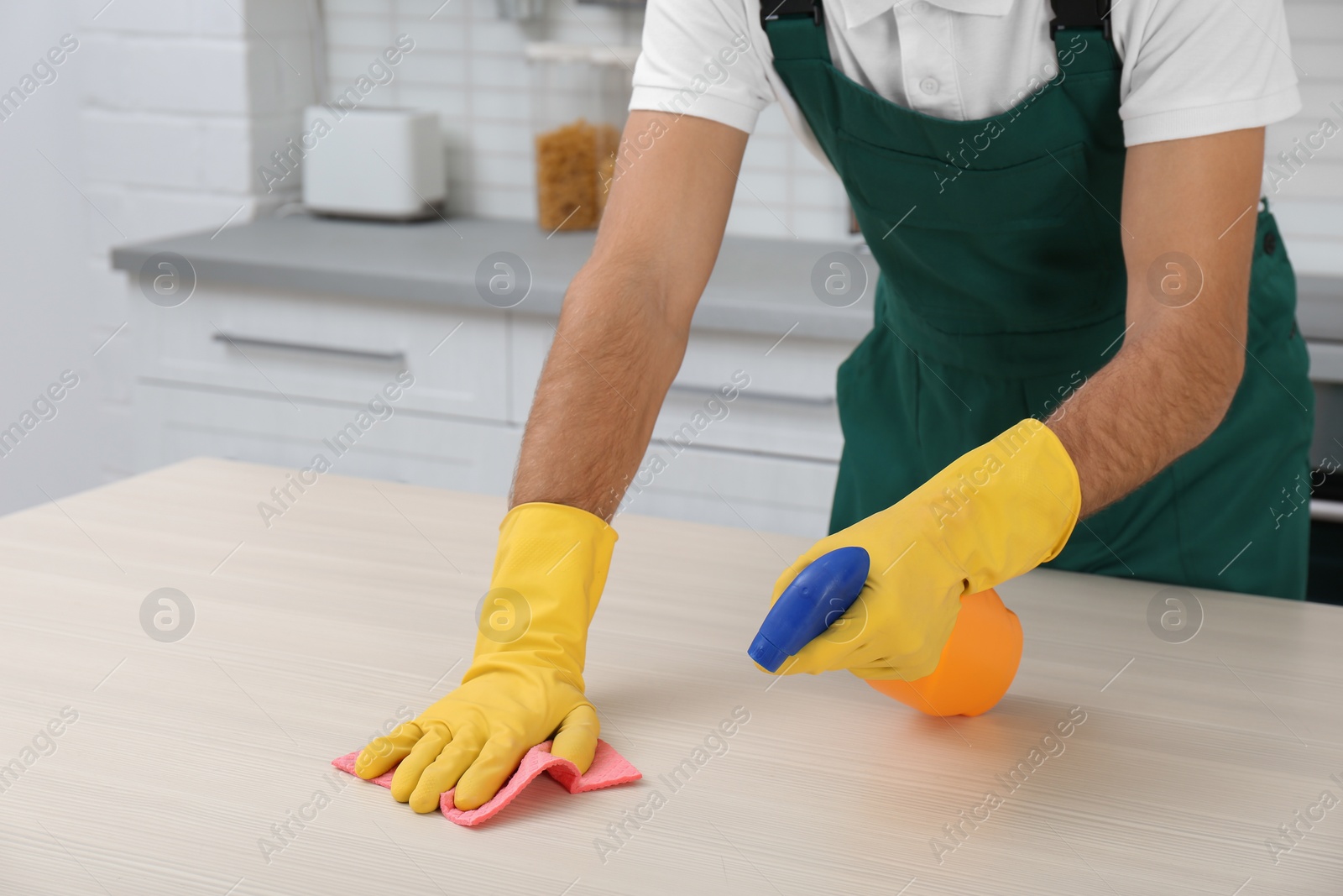 Photo of Male janitor cleaning table with rag in kitchen, closeup