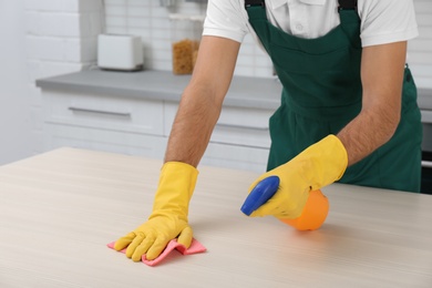 Photo of Male janitor cleaning table with rag in kitchen, closeup